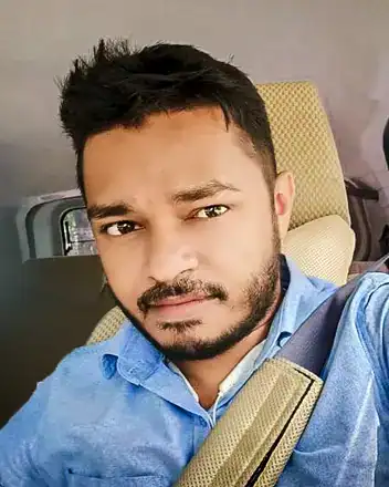 Home 53 A man with short hair and a beard, wearing a blue shirt and seated in a vehicle.